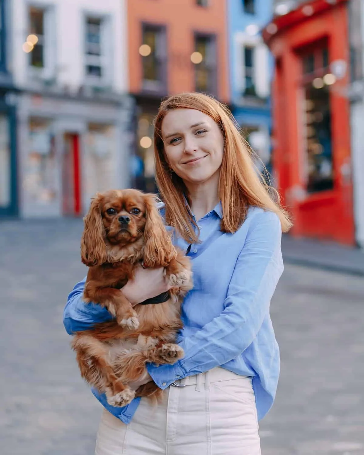 Katya smiling on Edinburgh’s Victoria Street, holding Steve, her ruby Cavalier King Charles Spaniel